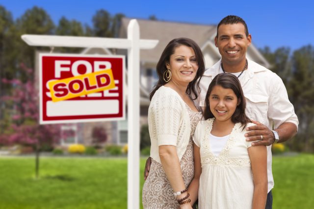 a man and woman standing in front of a for sale sign.